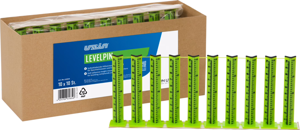 UZIN_Dummy_Levelpin_2026-02 Kartonirana kutija sa više jarko zelenih samolepljivih nivelacionih čepova; sprijeda je deset vertikalnih mernih traka na postolju povezane tankim žutim kanapom, na kutiji plavo-bela nalepnica sa natpisom 'LEVELPIN'.