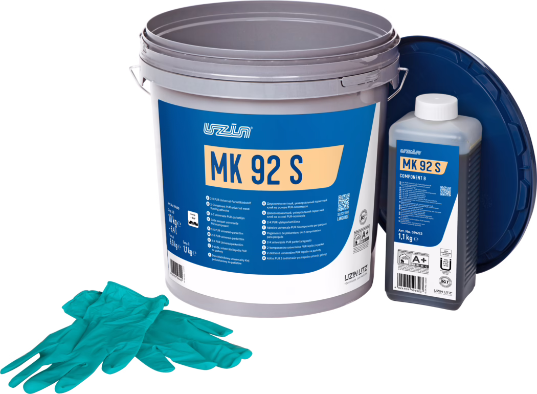 UZIN_Dummy_MK 92 S-10kg_2024-09 Studijsko proizvodno fotografisanje kompleta lepka za parket: velika siva plastična kanta sa upečatljivom plavom etiketom 'MK 92 S', desno manja pravougaona bočica označena 'MK 92 S Component B' sa belim čepom, a tamnoplavi poklopac naslonjen je pozadi. U prvom planu leži par tirkiznih jednokratnih rukavica. Predmeti su raspoređeni na beloj pozadini sa ujednačenim osvetljenjem, ističući detalje ambalaže i informacije o proizvodu za postavljanje podova.